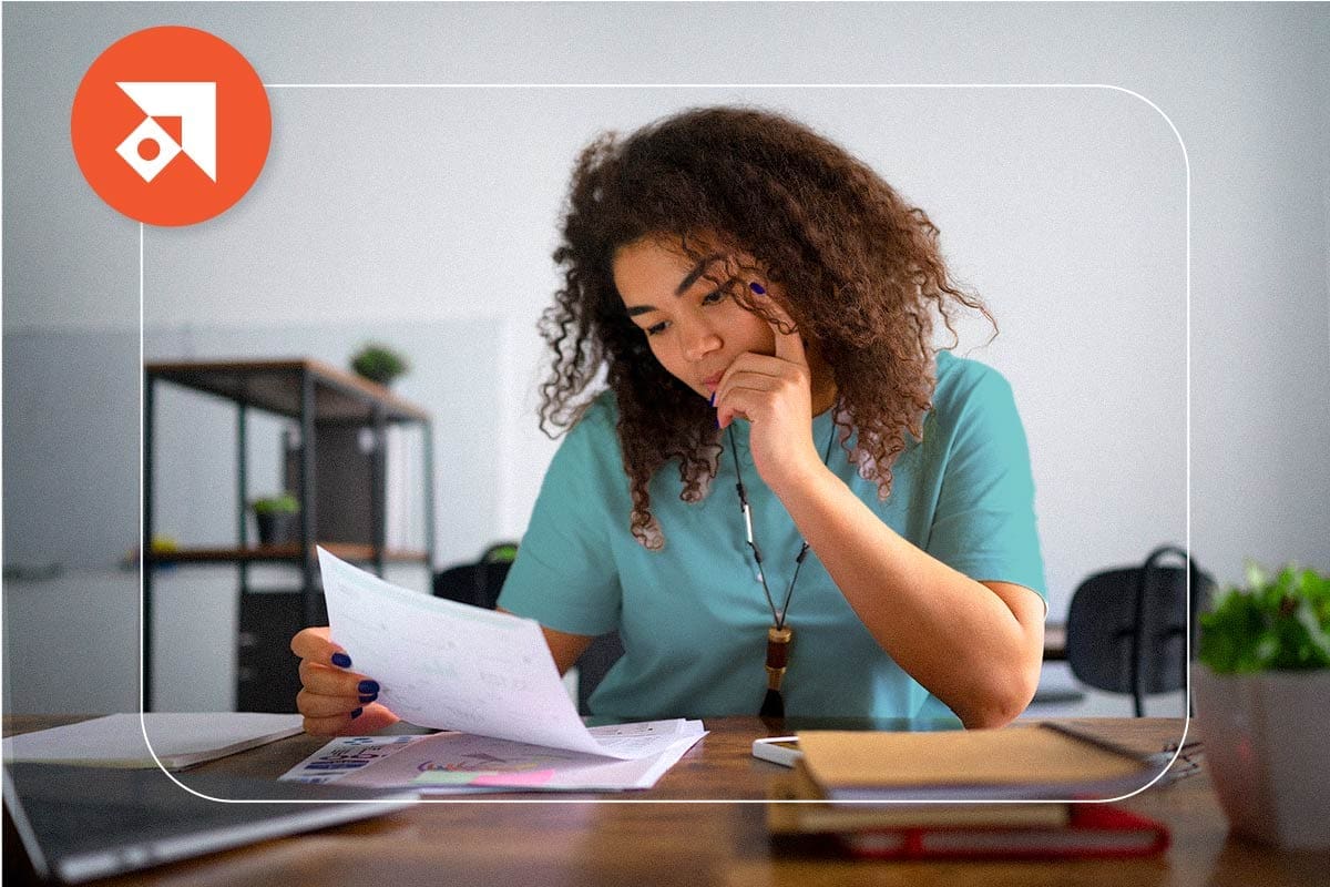 A nurse looking at paperwork at a table in front of a computer. With the text: 5 Reimbursement Gaps Impacting Revenue Performance